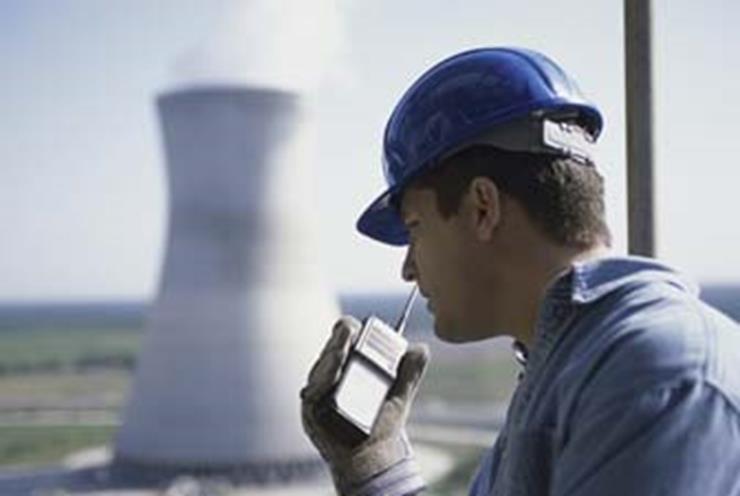 Side profile of a worker talking on a walkie-talkie at a power plant